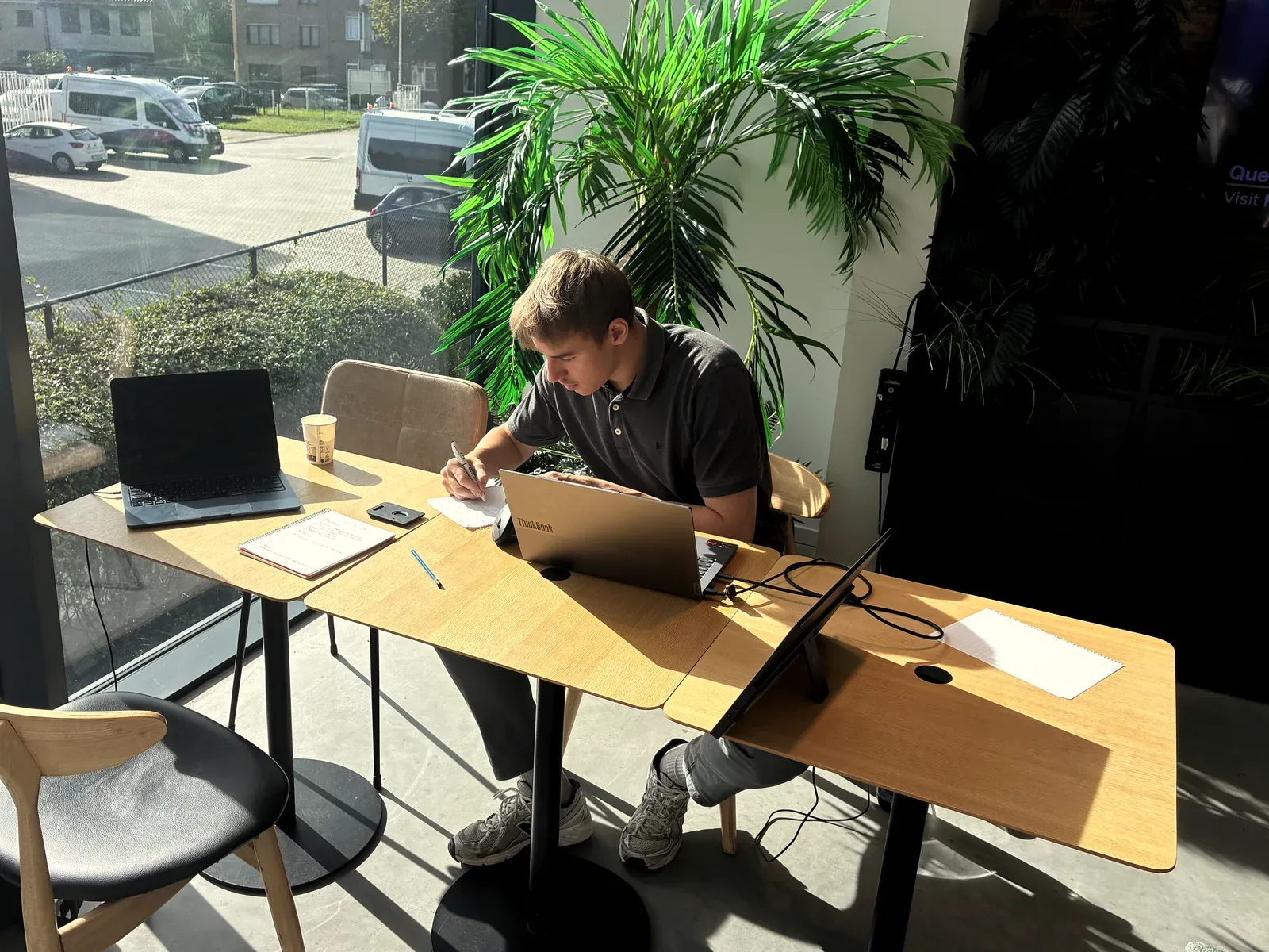 Siemen Vander Sande werkt aan een tafel bij het raam, met twee laptops en notities