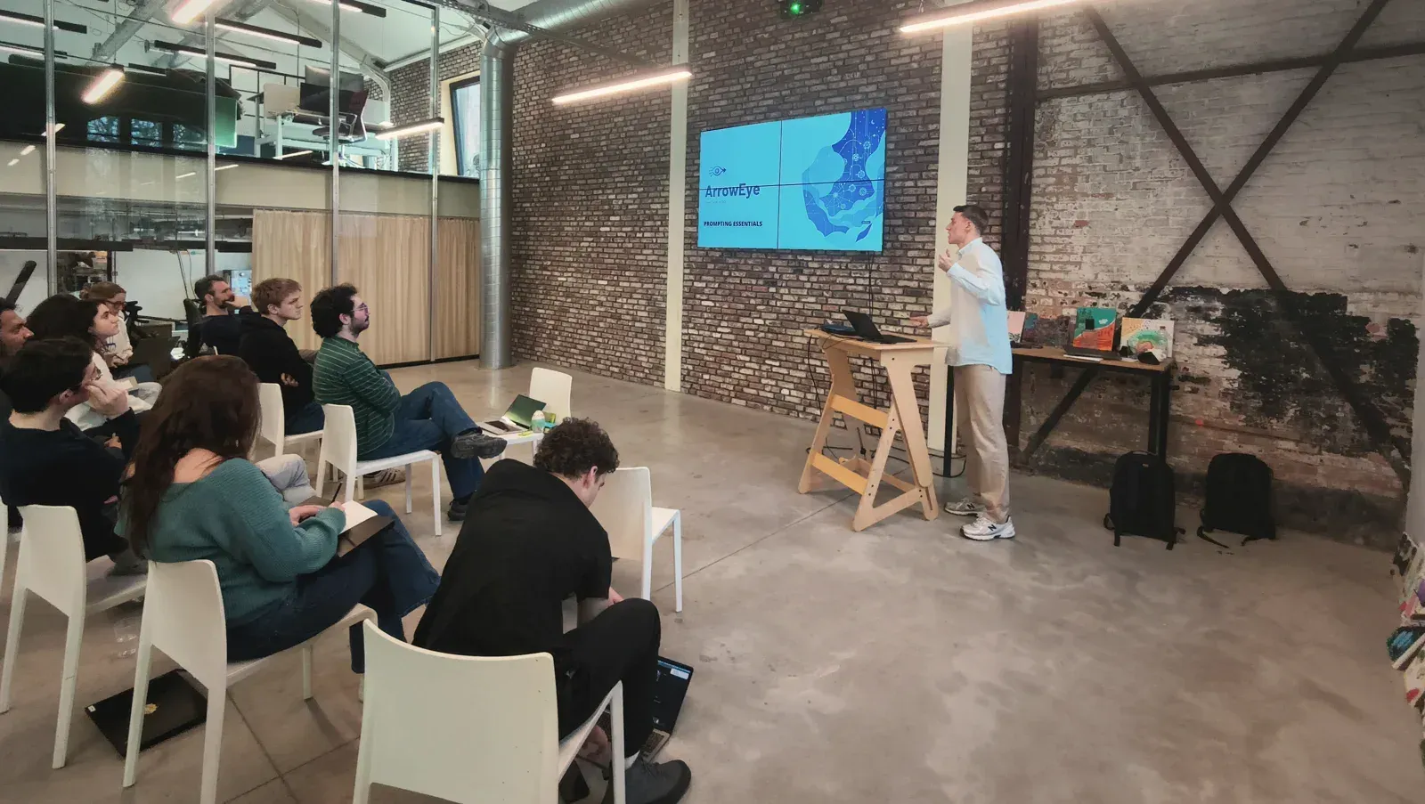 Participants follow an ArrowEye training in a loft; the trainer explains a slide on the screen